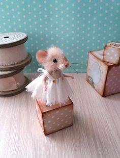 a toy mouse in a white dress on top of a wooden block next to some spools of thread