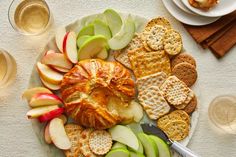 an assortment of crackers, apples and cheese on a plate with wine glasses next to it