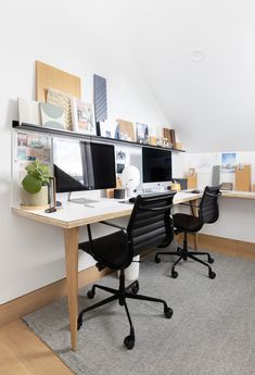 two computer monitors sitting on top of a wooden desk next to a black office chair