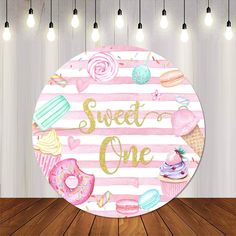 a round sign that says sweet one with donuts, cupcakes and other sweets