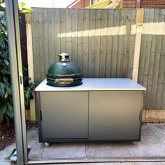 a large green grill sitting on top of a metal cabinet next to a wooden fence