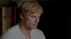 a young man with blonde hair and blue eyes stares into the distance while wearing a white shirt