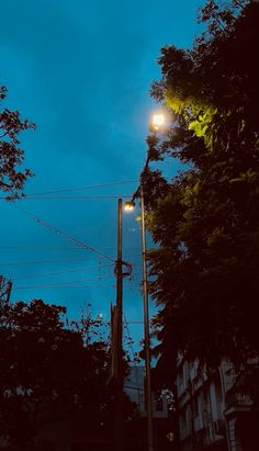 the street light is lit up in the dark sky above some trees and buildings at night