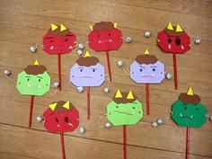 paper cutouts with faces on them sitting on top of a wooden table next to red and green sticks