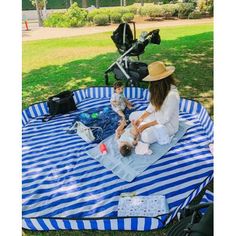 a woman and her baby sitting on a blue and white striped blanket in the park