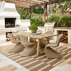 an outdoor dining table with chairs and a potted plant on the end, in front of a fireplace