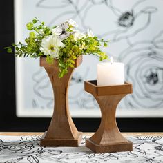 two wooden candlesticks with flowers in them on a white table cloth next to a black and white wall