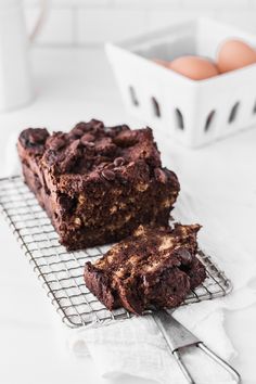 two pieces of chocolate brownie on a cooling rack with an egg in the background