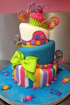 a multi - tiered cake decorated with colorful icing and bows on a blue plate