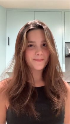 a woman with long hair standing in front of a kitchen counter smiling at the camera