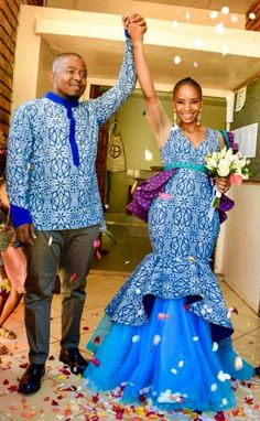 a man and woman in blue dresses holding hands while standing next to each other with confetti all around them