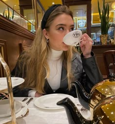 a woman sitting at a table drinking from a cup