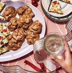 a person holding a glass of wine in front of a plate of cookies and desserts