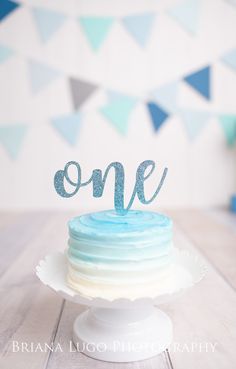 a blue and white cake with the word one on it sitting on top of a wooden table