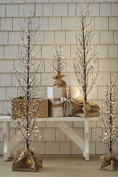 three small trees with white lights and wrapped presents on a bench in front of a house