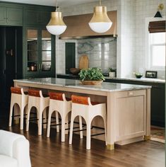 a kitchen with wooden floors and green cabinets, marble counter tops and gold pendant lights hanging from the ceiling