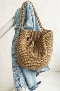 a crocheted handbag hanging on the back of a jean jacket with jeans underneath it