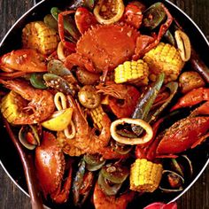 a pan filled with cooked crabs and corn on the cob next to two forks