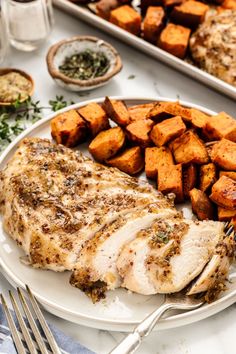 a white plate topped with meat and potatoes next to other food on top of a table