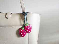 a white purse with two strawberries hanging from it's handle and attached to the side