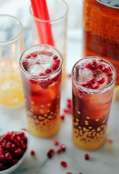 two glasses filled with ice and pomegranate on top of a white table