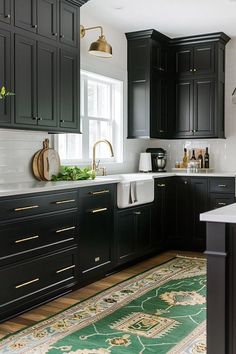 a kitchen with black cabinets and gold pulls on the sink, rug in front of it