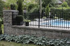 a pool behind a brick fence with plants growing on the side and in the foreground