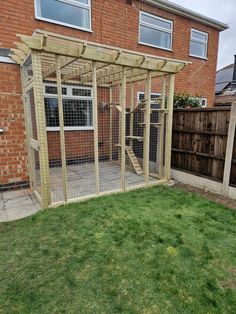 an outdoor area with a chicken cage and green grass in front of a brick building