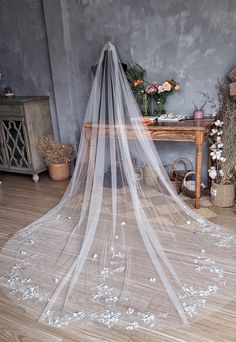 a wedding veil with white flowers on the floor in front of a table and chair