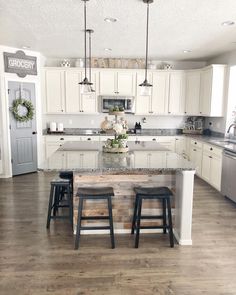 a large kitchen with white cabinets and marble counter tops, an island in the middle is surrounded by four stools