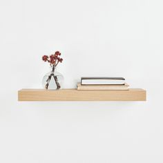 two books and a vase with flowers on a wooden shelf against a white wall,