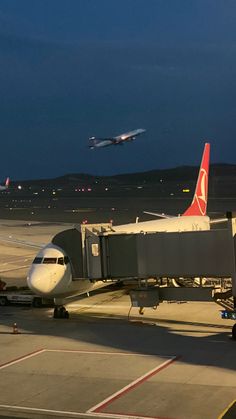 an airplane that is sitting on the tarmac with another plane in the air behind it