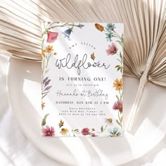 the wildflower is turning one birthday party card on top of a plate next to a fan