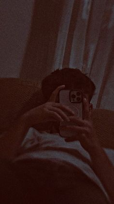 a person taking a photo with their cell phone in the dark, while lying on a bed