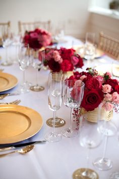 the table is set with gold plates, silverware and red flowers in vases