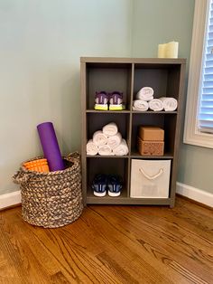 a shelf filled with lots of white towels and other items next to a basket on top of a hard wood floor