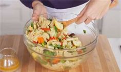 a woman mixing vegetables in a bowl with a wooden spoon on a cutting board next to an orange juice