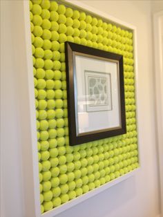 there is a picture frame on the wall with tennis balls in it and a black mat underneath