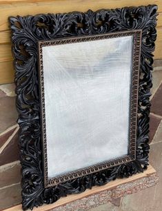 an ornate black framed mirror sitting on top of a stone floor