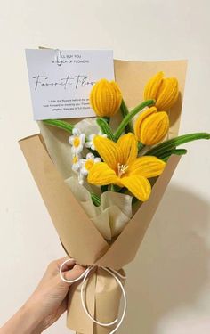 a hand holding a bouquet of yellow and white flowers with a note attached to it