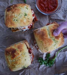 three sandwiches sitting on top of a piece of wax paper next to a bowl of ketchup