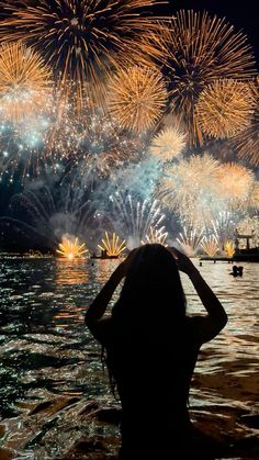 a woman standing in the water watching fireworks