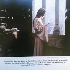 a woman standing in front of a window looking at her cell phone while wearing a robe