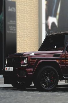 a red mercedes g - class parked in front of a building