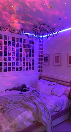 a bed with white sheets and purple lights in a room filled with pictures on the walls