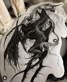 a black and white drawing of a demon on a plate with candles in the background