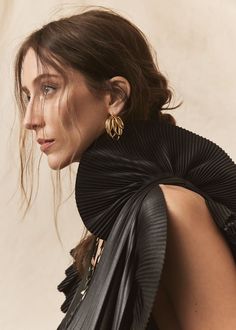 a woman in black dress with large gold earrings on her neck and shoulder, looking off to the side