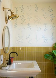 a sink and mirror in a room with yellow tiles on the walls, green plants painted on the wall