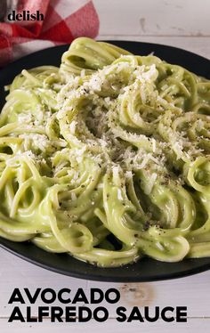 a black plate topped with pasta covered in pesto sauce