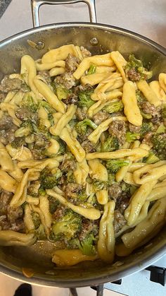 a pan filled with pasta and broccoli on top of a stove burner